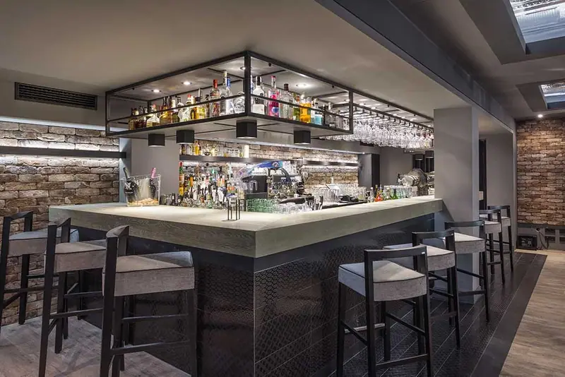Bar mit heller Theke, Barhockern und Stahlregal über dem Tresen