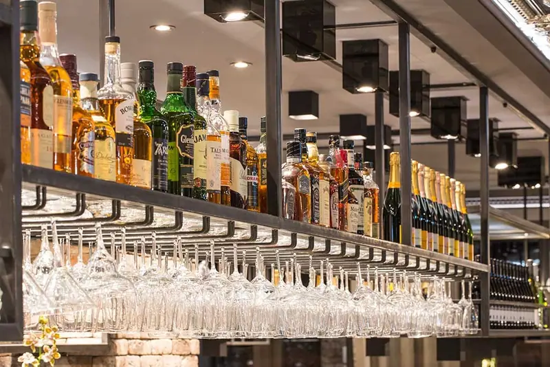 Stahlregal über der Bar mit hängenden Gläsern und Flaschen